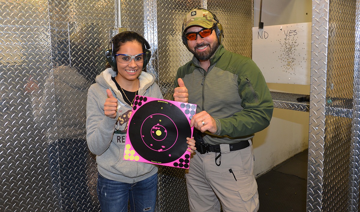 Woman with firearms instructor posing with target at an indoor shooting range