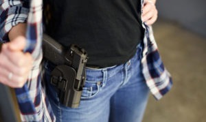 A women women her flannel to reveal a firearm on her hip.