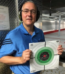 Photo of NSSF President and CEO Joe Bartozzi in a shooting bay at an indoor gun range posing showing the cameraman a freshly shot bullseye target.