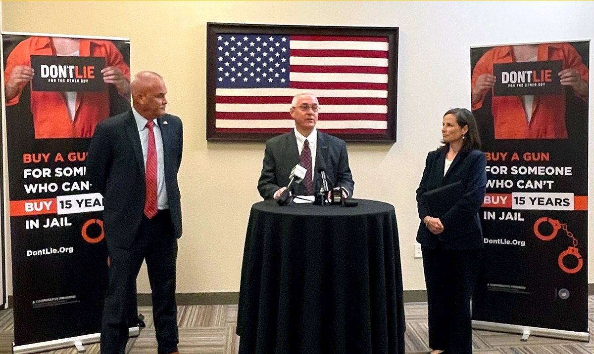 A photo of NSSF President and CEO Joe Bartozzi speaking at a Don't Lie for the Other Guy press conference in Fort Worth, Texas. Joe is Standing behind a black podium, flanked by representatives from the Bureau of Alcohol, Tobacco, Firearms and Explosives (ATF) and the Department of Justice (DOJ). A framed American flag hangs from the wall behind Bartozzi and is flanked by tall vertical banners branded with the logo of Don't Lie campaign and the message - Buy a gun for someone who can't, buy 15 years in Jail - Dont:ie.org. The campaign targets illegal gun purchases.